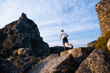 A trail runner running along a mountain ridge under a blue sky on Table Mountain in Cape Town - 397566139