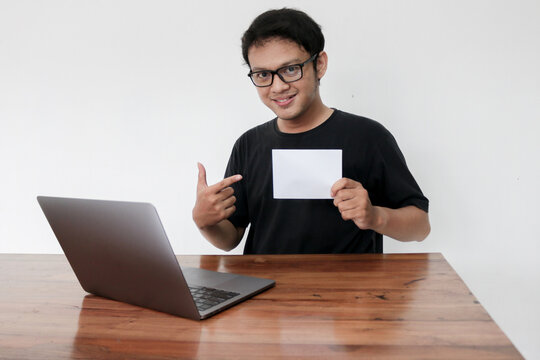 Young Asian man feeling happy with laptop and holding empty white space paper. Smile Indonesia Man wear black shirt Isolated grey background.