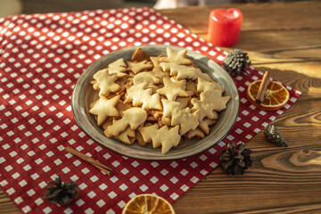A plate of delicious homemade holiday shaped cookies on a red tablecloth on a wooden table. Concept of creating a cozy atmosphere and festive mood