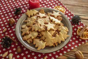 A plate of delicious homemade holiday shaped cookies on a red tablecloth on a wooden table. Concept of creating a cozy atmosphere and festive mood