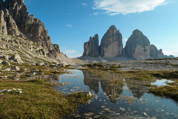 Fototapeta na wymiar A panoramic view on the famous Tre Cime di Lavaredo (Drei Zinnen), mountains in Italian Dolomites. The mountains are reflecting in small paddle. Desolated and raw landscape. Natural phenomenon