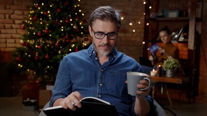 Couple reading book at home at Christmas in winter, dark room with Christmas tree.