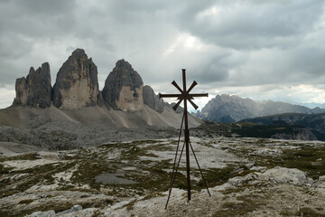 A metal cross with the view on the famous Tre Cime di Lavaredo (Drei Zinnen) in Italian Dolomites. The mountains are surrounded by thick clouds. Spirituality and achievement. Natural wonder.