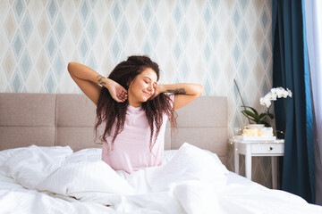 Font view of young woman waking up in early morning sitting on bed with whitesnow linen and sretch...