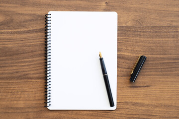 Blank notebook with pen is on top of wood office desk table. Top view, flat lay.