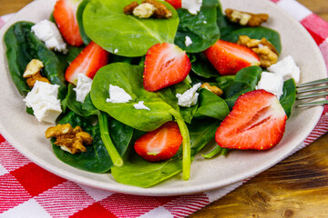 Fresh healthy salad with strawberry, spinach, walnuts and feta cheese on wooden table