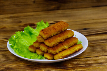 Fried fish fingers on a plate with lettuce on wooden table