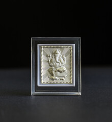 Tiny embossed silver Ganesha frame on black background. Hindu idol photo made with precious metal as gift items.