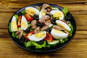 Tasty tuna salad with lettuce, black olives, eggs and fresh vegetables on wooden table