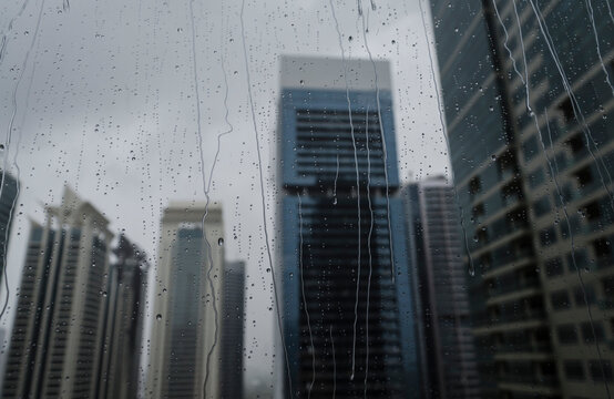 A blur view of office towers through wet window glass pane. Abstract photo of modern building during rainy season.