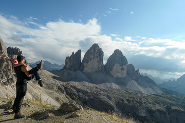 A man holding a woman in his arms on top of Sextner Stein and enjoying the view on the famous Tre Cime (Drei Zinnen) in Italian Dolomites. Desolated and raw landscape, full of lose stones. Love