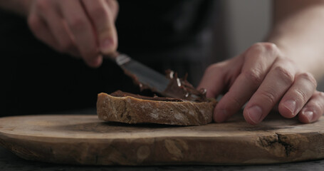 man spreading chocolate hazelnut spread on ciabatta slice on wood board