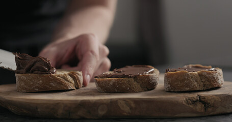 man spreading chocolate hazelnut spread on ciabatta slice on wood board