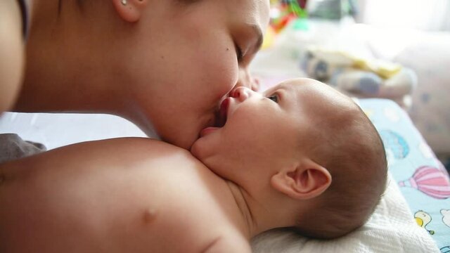 Authentic close up shot of young mother is playing and kissing with her newborn baby. Concept of motherhood.