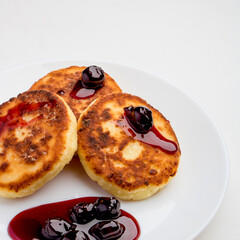 Cheesecakes with cherry jam on a white plate on a white plate.