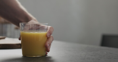 man hand take orange juice in thin glass from countertop
