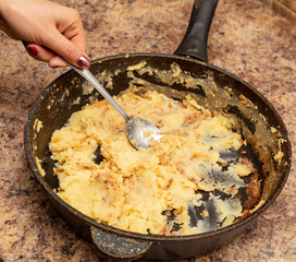 Spoon in hand stirring potatoes in a frying pan.