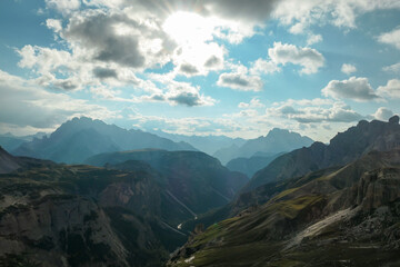 Naklejka premium A panoramic view on a vast valley in Italian Dolomites. The valley is surrounded with high mountains from each side. There are a few clouds above. Remote and isolated place. Remedy