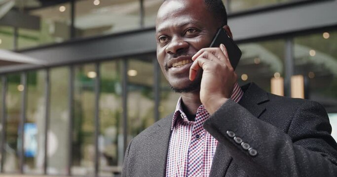 Surprised excited black man businessman hold smartphone listening good news amazed by phone call making a deal, happy African guy answering the cellphone call overjoyed by deal success in urban city