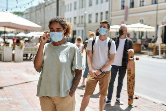 Young African American Woman Wearing Mask Standing With Other People In Line, Respecting Social Distancing To Enter Takeout Restaurant During Coronavirus Lockdown