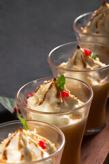 Four Crem covered caramel in glasses with berryes in a line on a wooden plate