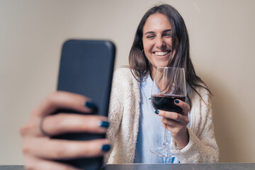 young woman smiling and clinking online with red wine having a video call with her friends online...