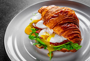 Croissant sandwich with poached egg, tomato and avocado on plate
