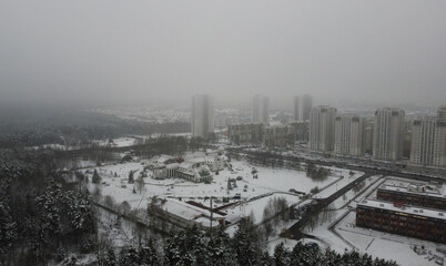 Top view of winter snowy city near forest on foggy evening