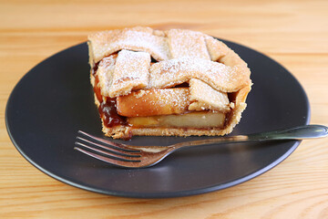 Slice of delicious homemade fresh apple pie on black plate served on wooden table