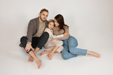 Portrait of attractive father, daughter and mother embracing together in front of grey background.