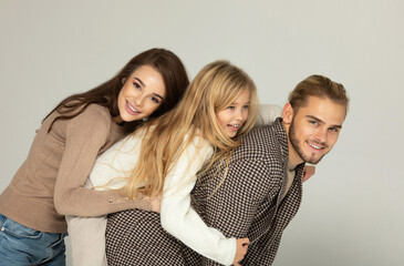 Portrait of attractive father, daughter and mother embracing together in front of grey background.