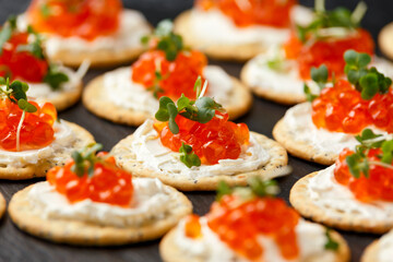 Salmon caviar and soft cheese savory crackers with sesame and poppy seeds served on black slate board