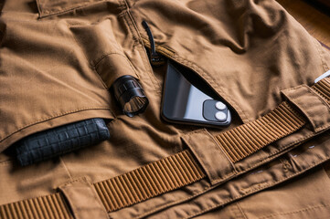 EDC concept on coyote tactical pants. Everyday carry with flashlight, foldable knife, wallet and smartphone. - obrazy, fototapety, plakaty