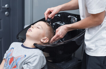 Obraz na płótnie Canvas the process of washing head a blond boy in a chair in a barbershop salon, a barbershop concept for men and boys