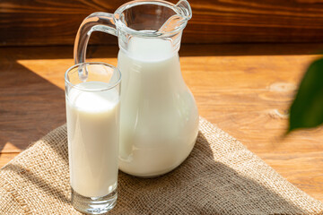 Glass pitcher of milk on old wooden table