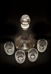 Glass transparent decanter and four glasses close up on a black background