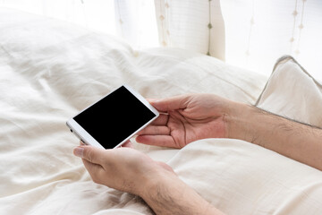 ベッドでリラックスしスマートフォンを使う男の手元