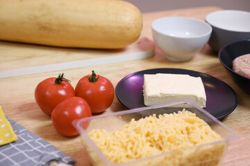 A set of fresh vegetables on a wooden kitchen table for cooking. Onions, garlic, red tomato and cheese on the table.