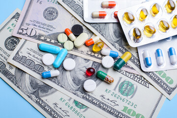 Colorful pills and capsules on dollar money on light blue background. Medicine expenses, high costs of medication concept, close up.