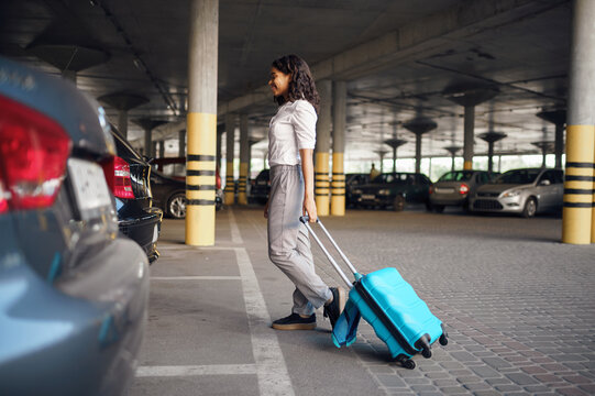 Young woman with suitcase in car parking