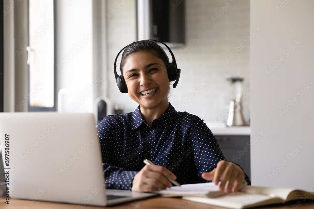 Canvas Prints Remote job or learning. Portrait of happy young mixed race female working from home in headset using laptop. Excited indian lady wearing earphones looking at camera studying via social media platform