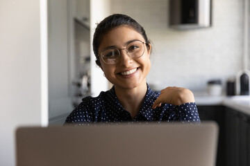 Working at home office. Portrait of happy smiling young indian female in stylish glasses sitting by...