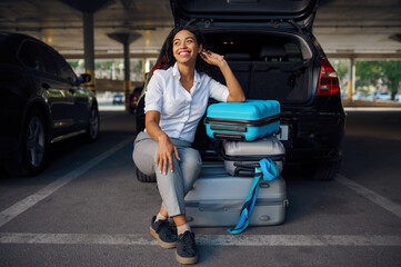 Happy woman sitting on suitcases in car parking