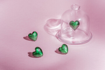 green heart on a pink background. green heart under a glass transparent cover on a pink background. levitation of glass heart on pink background