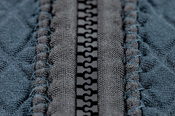 A macro shot of a closed, plastic zipper in a modern blue garment.