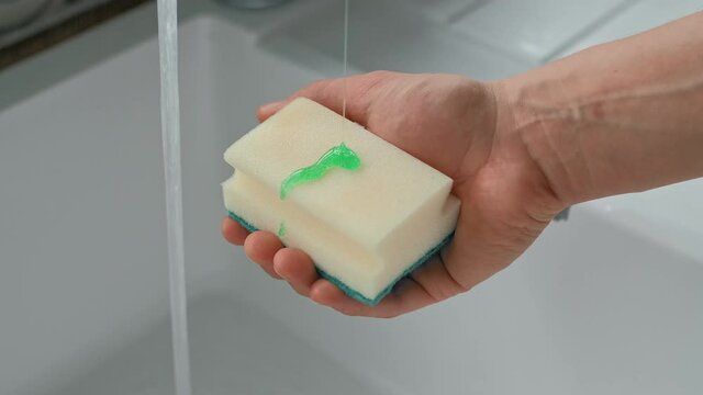 Man holding a kitchen sponge with dishwashing liquid pouring on it