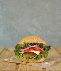 Cheeseburger with tomatoes, red onions and lettuce on a wooden background. Unhealthy food