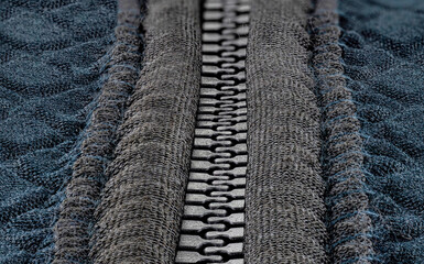 A macro shot of a closed, plastic zipper in a modern blue garment.