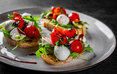 Italian bruschetta with roasted tomatoes, mozzarella cheese, balsamic vinegar and herbs on plate