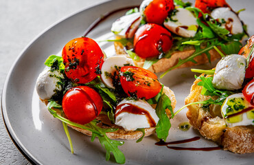 Italian bruschetta with roasted tomatoes, mozzarella cheese, balsamic vinegar and herbs on plate